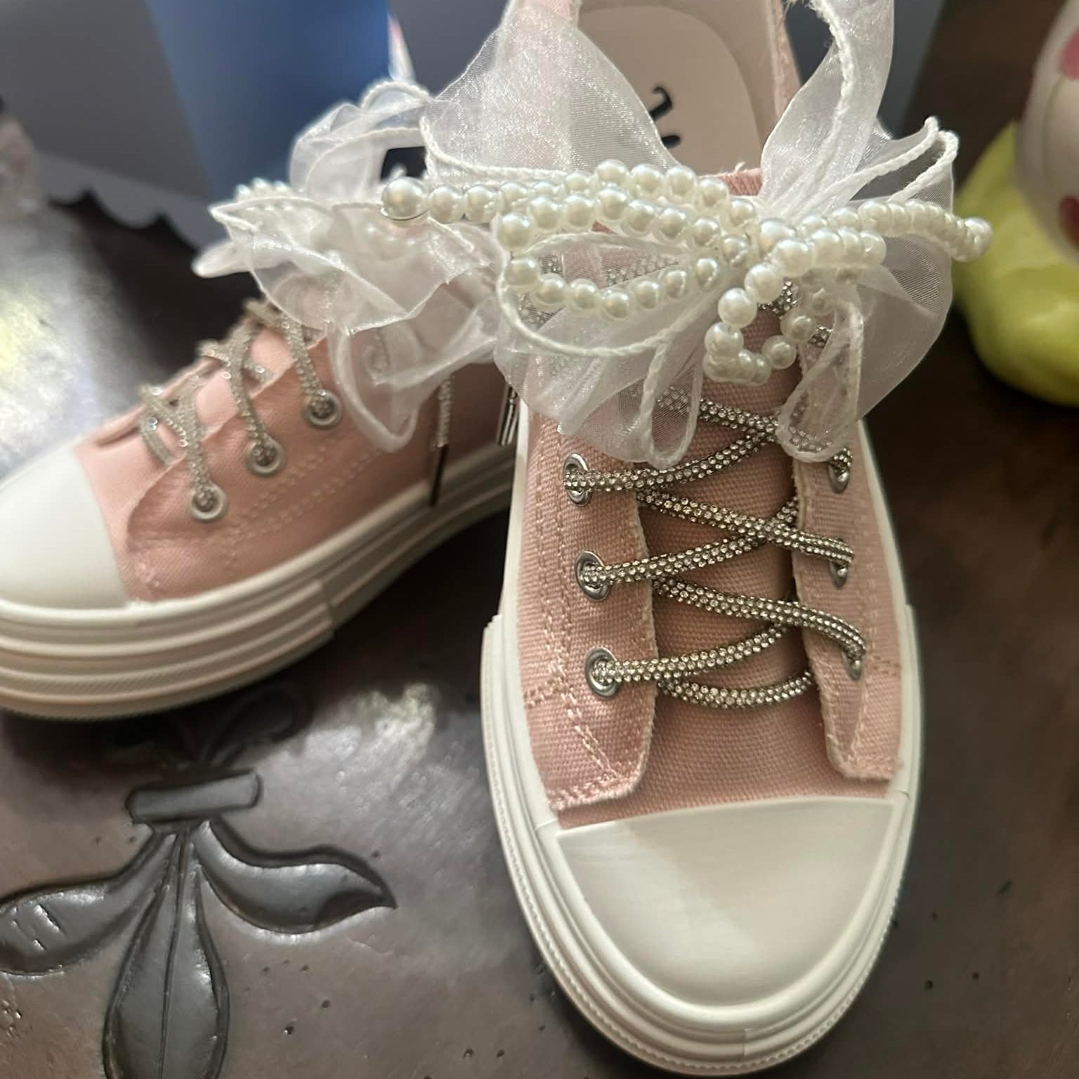 Pink sneakers with decorative lace and pearls on a wood surface