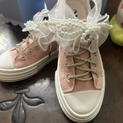 Pink sneakers with decorative lace and pearls on a wood surface